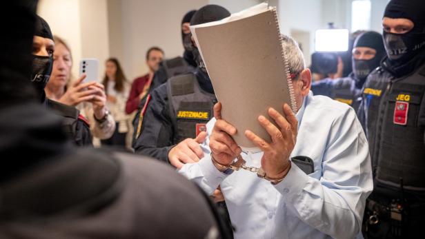 Khaled H. verdeckt sein Gesicht mit einer Mappe, er ist umringt von Polizeibeamten.