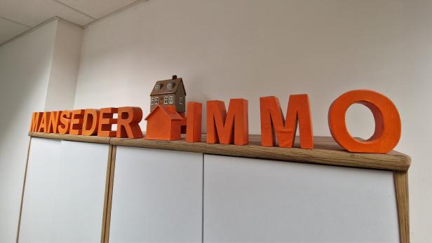 Schriftzug von Manseder Immobilien mit Hausmodellen im Unternehmensbüro.