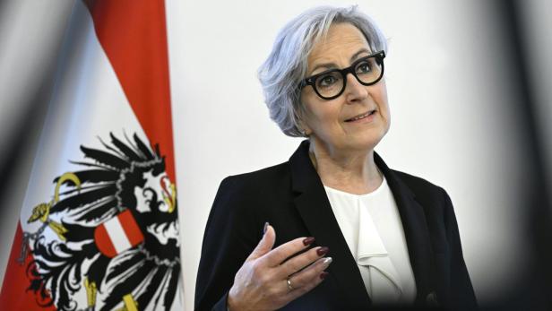 Die österreichische Justizministerin Anna Sporrer spricht vor einer österreichischen Flagge.