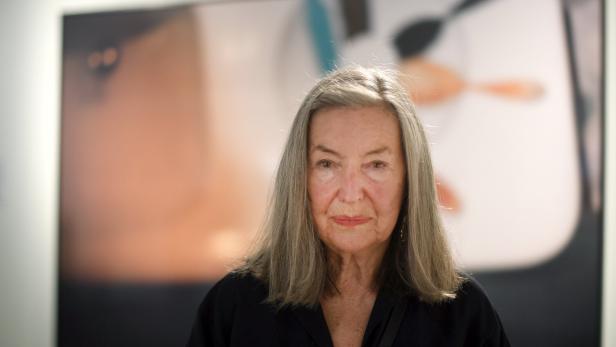 Die Fotografin Elfie Semotan blickt ernst in die Kamera, im Hintergrund unscharf ein buntes Kunstwerk