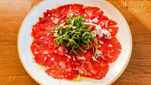 Das Bild zeigt ein Rinder-Carpaccio mit Parmesan, Olivenöl und Rucola