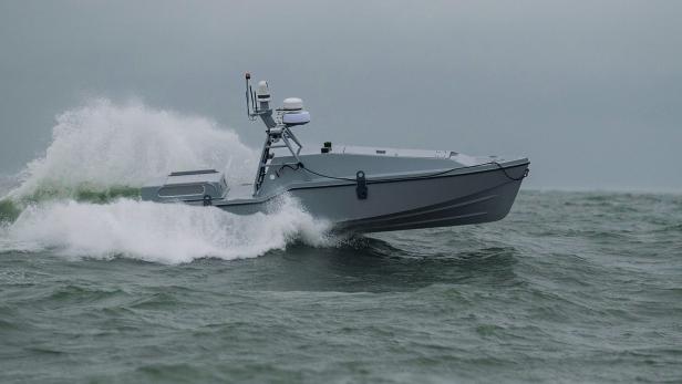 Eine "Corsair"-Drohne (ein graues Motorboot, mit auffälligem Radarsystem) fährt auf dem Wasser und hinterlässt eine große Welle hinter sich.