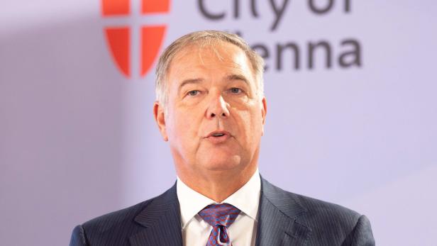 Ein älterer Mann im Anzug spricht gestikulierend vor einem Hintergrund mit der Aufschrift „City of Vienna“.