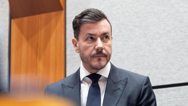 Mann in dunkelblauem Anzug vor hellem Hintergrund.