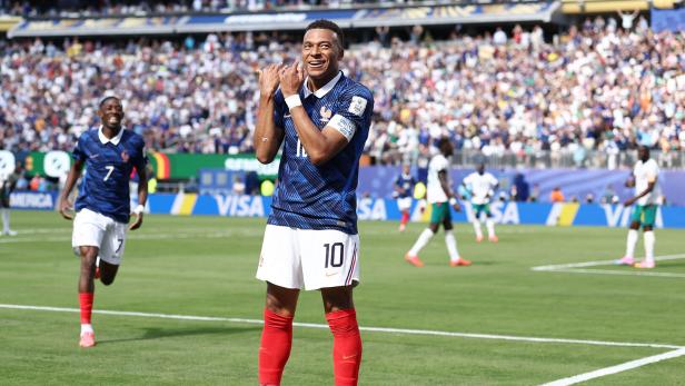 Kylian Mbappe steht auf dem Fußballplatz und jubelt über ein Tor, indem er eine Flötenbewegung macht