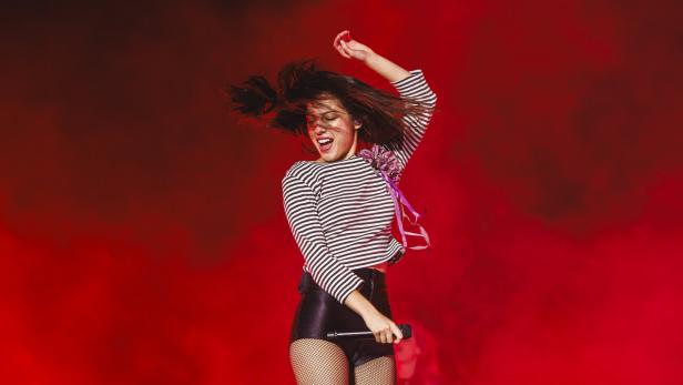 Popstar Olivia Rodrigo springt auf der Bühne vor rot beleuchteten Trockeneisschwaden. 