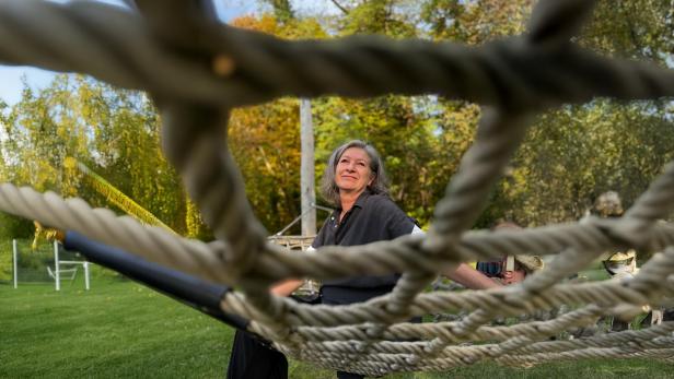 Frau sitzt auf einem Kletternetz im Freien und blickt lächelnd in die Ferne.