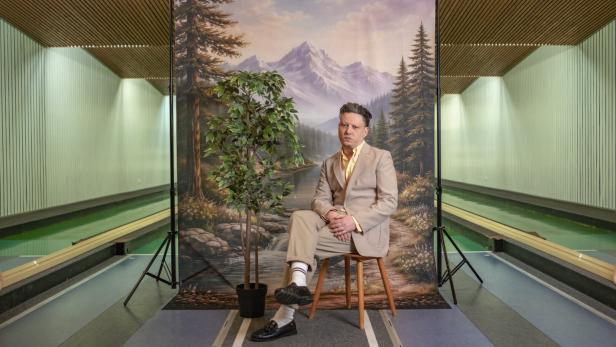 Der Musiker Konstantin Gropper im hellen Anzug, vor einer großformatigen gemalten Wald- und Bergszenerie