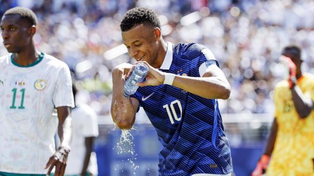 Kylian Mbappe schüttet sich während eines Fußballspiels Wasser aus einer Trinkflasche auf den Arm