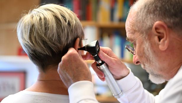 Ein Arzt untersucht mit einem Otoskop das Ohr einer Patientin in einer Praxis.