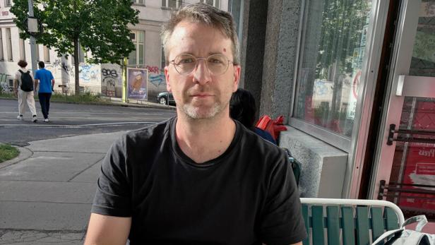 Ein Mann mit Brille und schwarzem T-Shirt sitzt vor einem Schmalzbrot und einem großen Bier
