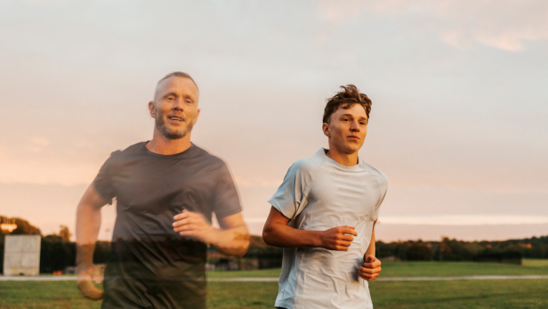 Zwei Männer joggen nebeneinander auf einer offenen Wiese unter bewölktem Himmel