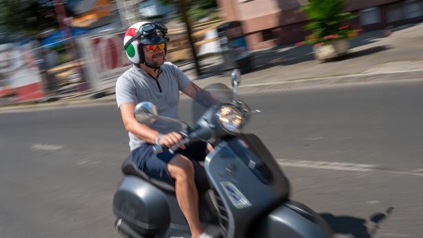 Ein Mann fährt auf einem Roller mit Helm durch eine Straße.