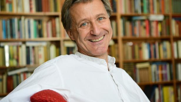 Der Kulturmanager und Autor Sven Hartberger in weißem Hemd, lächelnd, vor einer Bibliothek