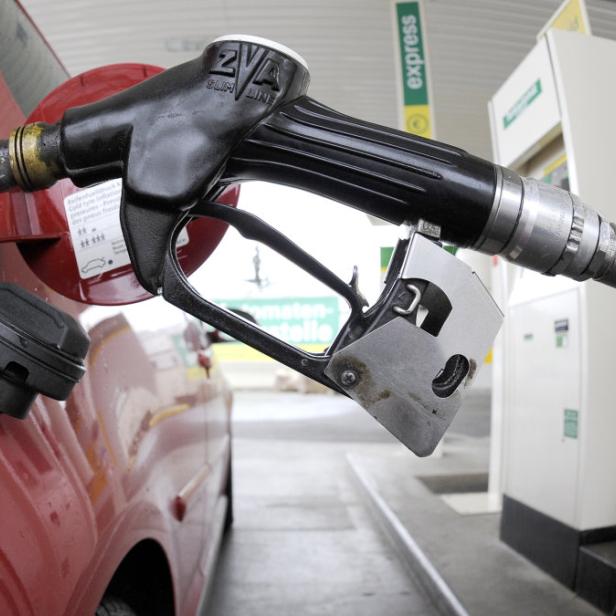 Eine Zapfpistole steckt in einem roten Auto an einer Tankstelle.