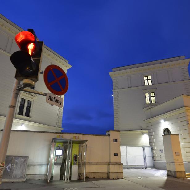 Eine rote Fußgängerampel vor zwei weißen Gebäuden in Wien bei Nacht.