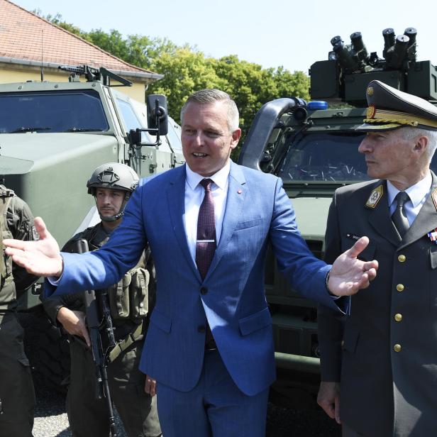 Mario Kunasek und ein Offizier stehen vor Militärfahrzeugen, flankiert von Soldaten.
