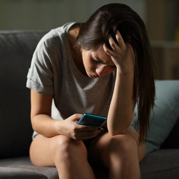 Eine junge Frau schaut traurig auf ihr Handy.