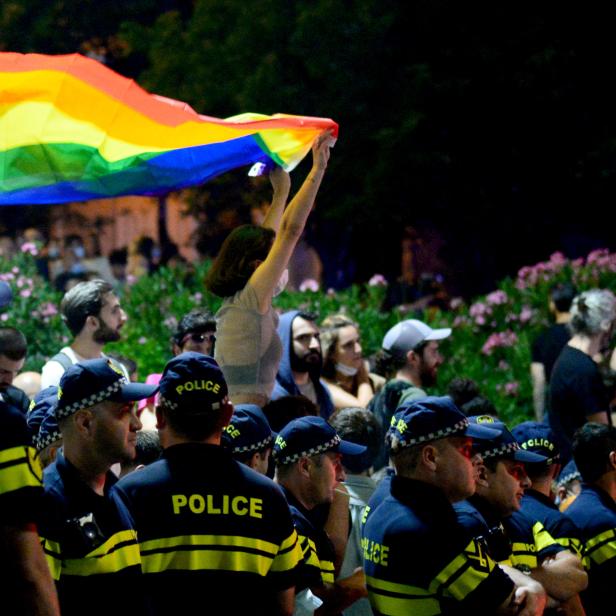 Eine Teilnehmerin einer Kundgebung hält zwischen Polizist:innen eine Regenbogen-Flagge. Tausende haben in Tiflis demonstriert, nachdem am 5. Juli gewaltbereite Gruppen die LGBTIQ-Community und Journalist:innen attackiert hatten.