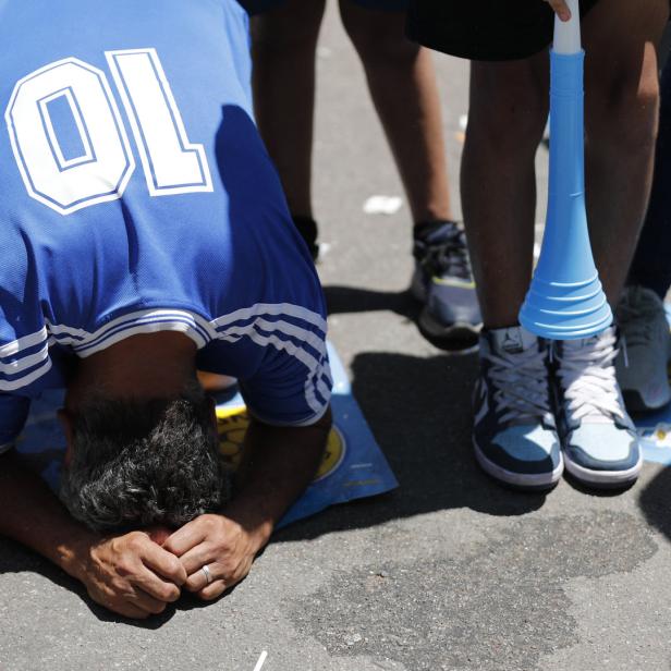 Ein Mann im Argentinien-Trikot kniet auf der Straße, eine Tröte liegt daneben.