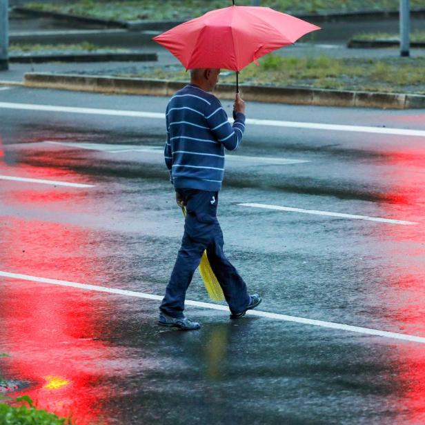 Mann geht mit Regenschirm über eine Straße