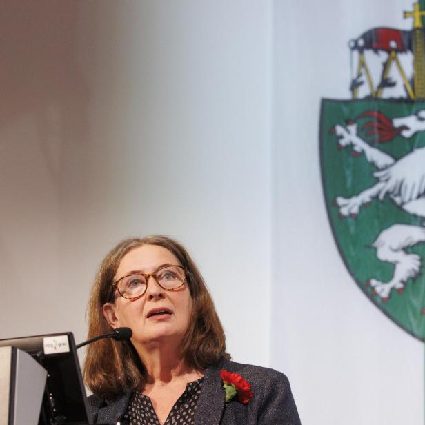 Elke Kahr, Bürgermeisterin von Graz, bei einer Rede. Dahinter das Wappen der Steiermark