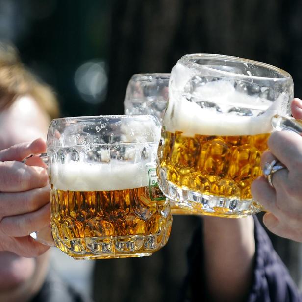 Eine Gruppe an Menschen stoßen mit halbvollen Bierkrügen an.