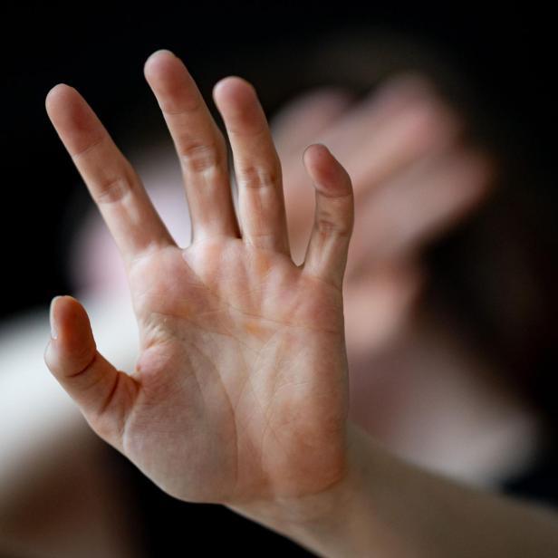 Eine linke Hand in schützender Abwehhaltung, dahinter verdeckt die rechte Hand das Gesicht einer Frau. Symbolbild zu Gewalt an Frauen