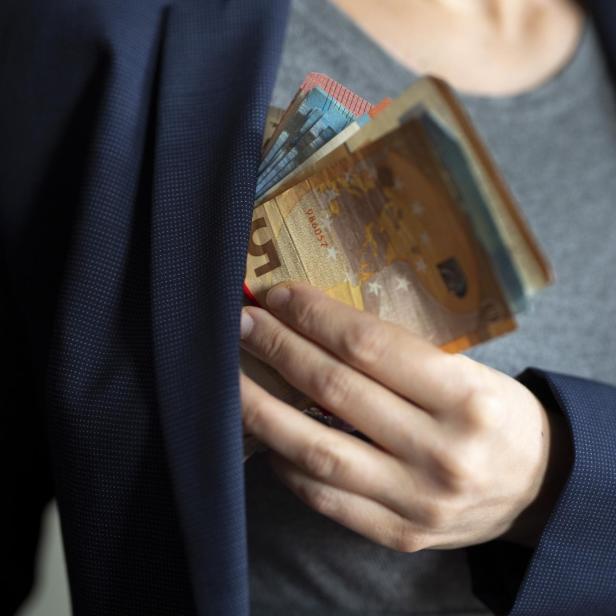 Eine Person steckt einen Stapel Euroscheine in die Innentasche eines blauen Sakkos.