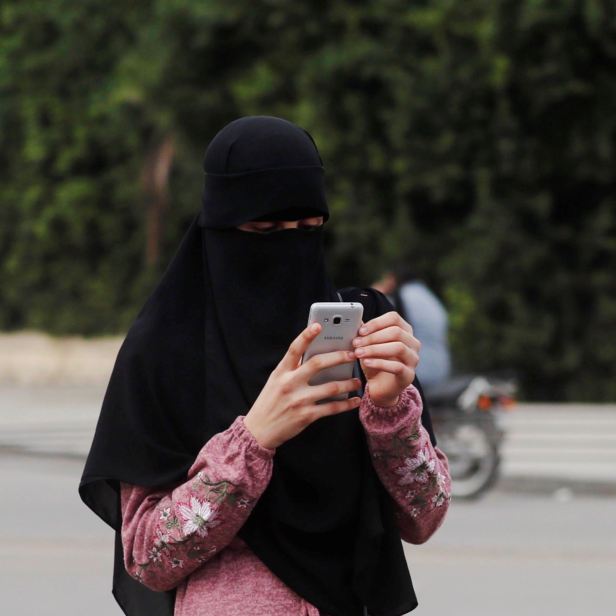 Mädchen mit Kopftuch hält Handy in der Hand