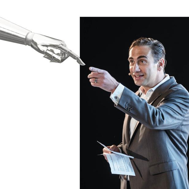 Ein Mann im Anzug gestikuliert in Richtung eines Roboterarms.