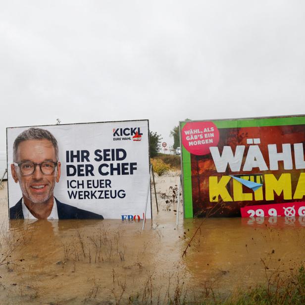 EIn Plakat von Herbert Kickl, wo draufsteht "Ihr seid der Chef" und ein Grünen-Plakat mit der Aufschrift "Wähl Klima" stehen im Hochwasser 