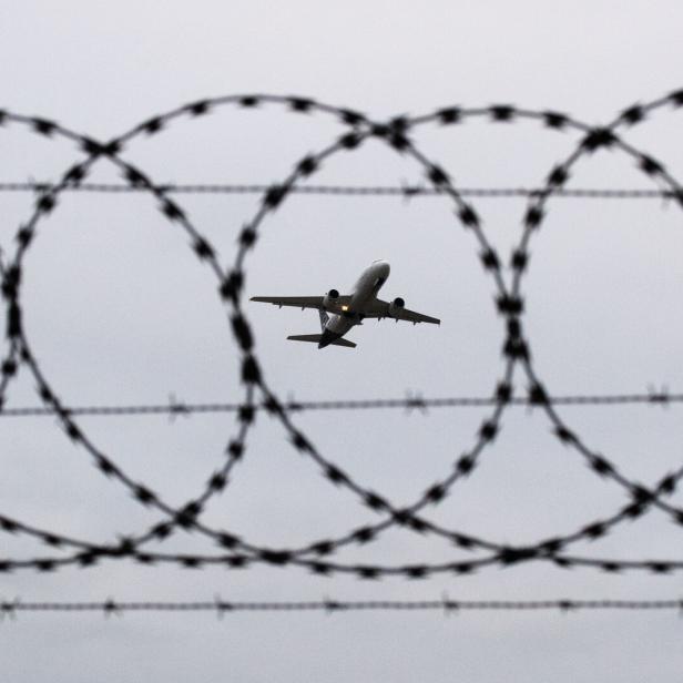 Ein Stacheldrahtzaun im Vordergrund mit einem Flugzeug im Hintergrund