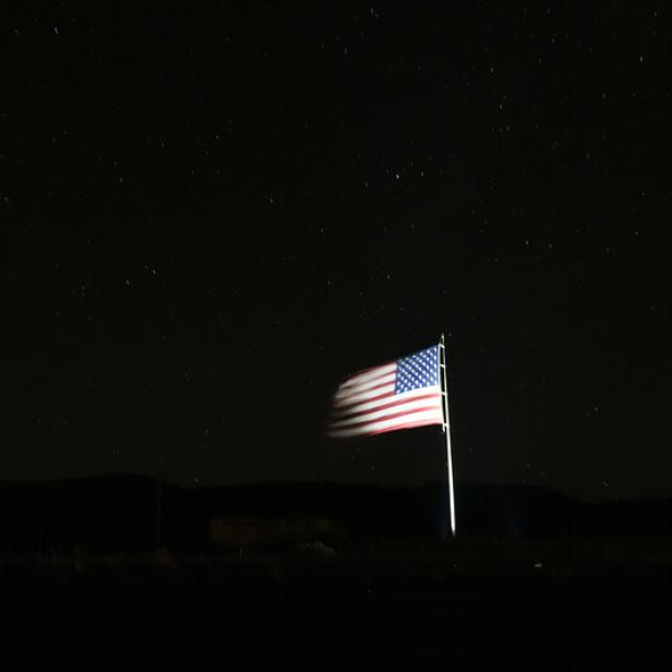 A starry sky is visible as a large U.S. flag waves in the wind along Route 69 in Mayer, Ariz., the night before Americans will vote in the 2024 presidential election, Monday, Nov. 4, 2024. (AP Photo/Julio Cortez)