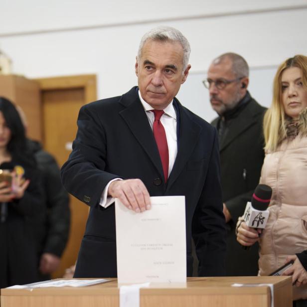 Călin Georgescu steht vor einer Wahlurne mit einem Stimmzettel in der Hand.