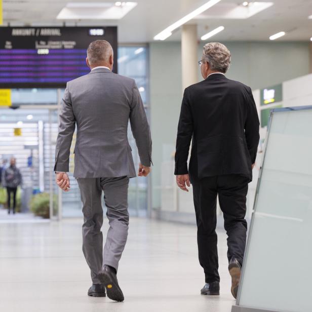 Landeshauptmann Mario Kunasek (FPÖ) (li.) und sein Vorgänger Christopher Drexler (ÖVP) (re.) sind von hinten zu sehen. Beide tragen Anzug und schreiten nebeneinander vom Betrachter weg.