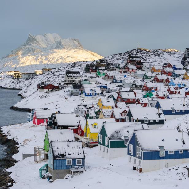 Bunte Häuser bedeckt mit Schnee in einer Küstenstadt mit Bergen im Hintergrund.