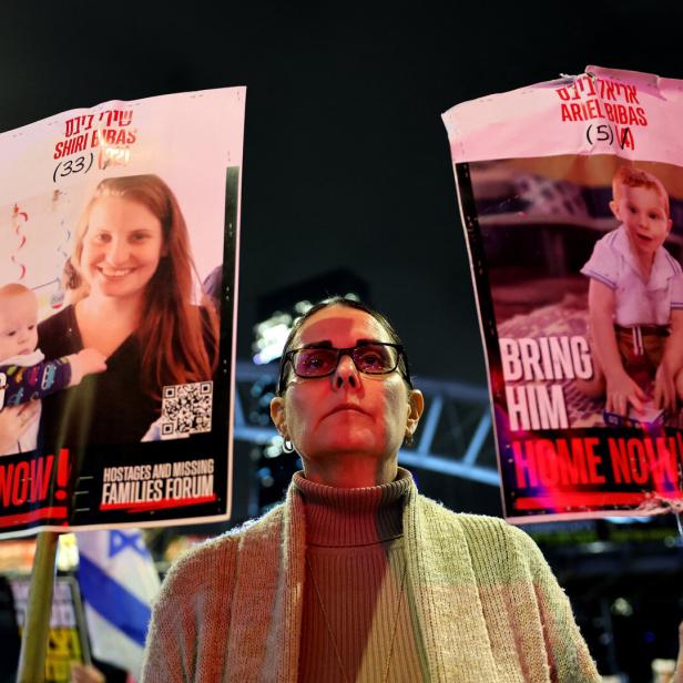 Eine Frau demonstriert mit Schildern, die Fotos von Shiri Bibas und Ariel Bibas zeigen, mit der Aufschrift „Bring sie/ihn jetzt nach Hause!".