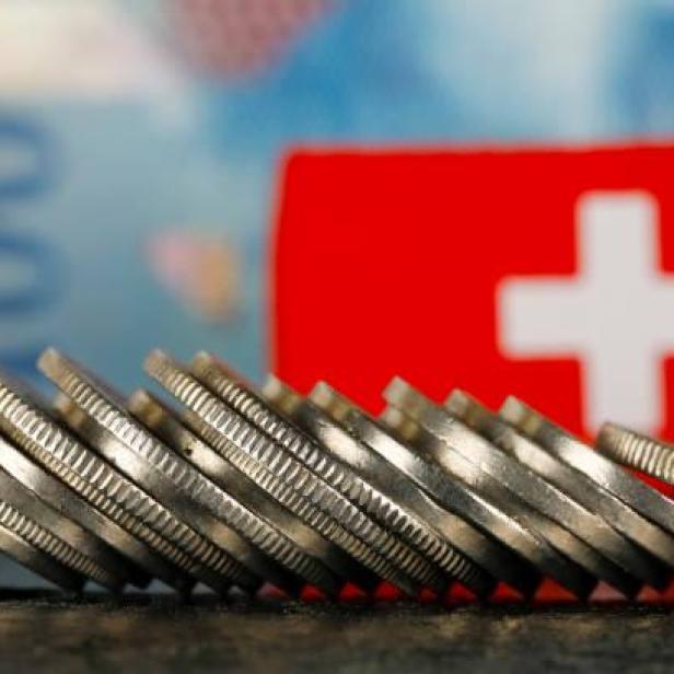 Bild von einem umgefallenen Stapel mit Münzen. Im Hintergrund sieht man die Schweizer Flagge und Geldscheine.