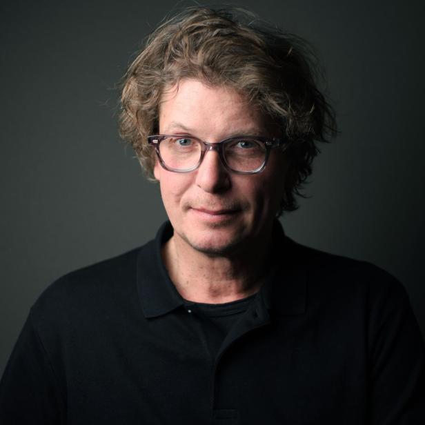 Porträt von Wolfgang Paterno mit Brille vor einem dunklen Hintergrund.