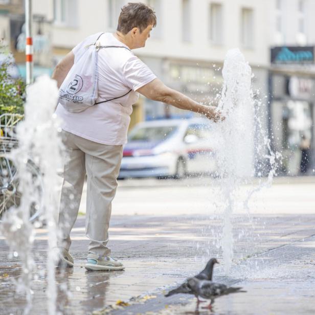 Ein Frau erfrischt sich bei Hitze an einem Brunnen.