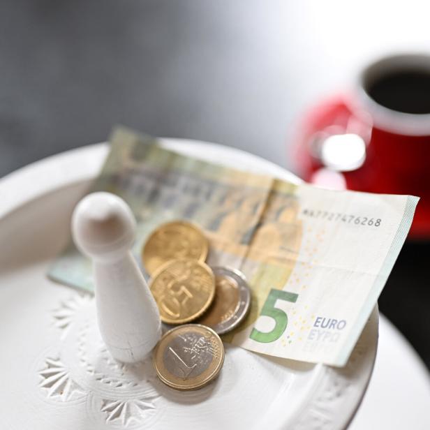 Trinkgeld, Geld und ein Spielstein liegen auf einem Teller, im Hintergrund eine rote Tasse.