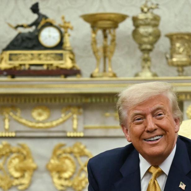 Trump lächelt, hinter ihm goldene Schmuckstücke.