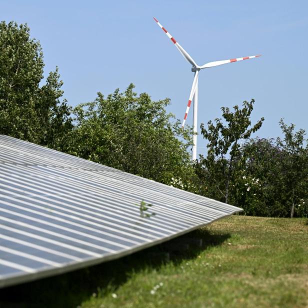Auf dem Bild befindet sich eine Photovoltaikanlage und eine im Hintergrund ein Windrad