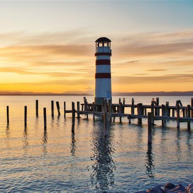 Ein rot-weißer Leuchtturm am Ufer des Neusiedlersees im Sonnenuntergang