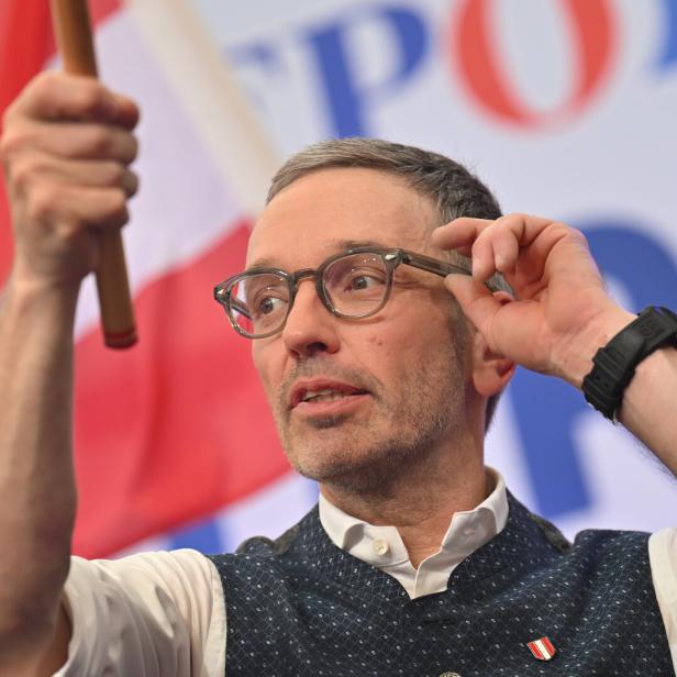 Herbert Kickl hält eine Österreich-Fahne in der Hand und greift sich an die Brille 
