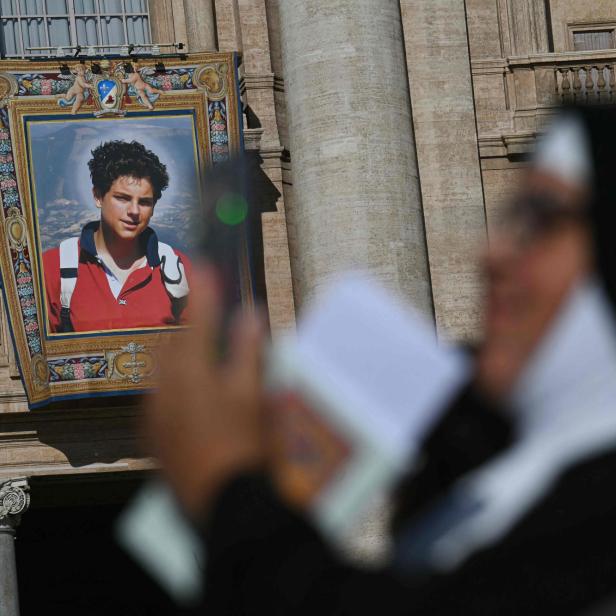 Eine Nonne schaut auf ihr Handy, während im Hintergrund ein Porträt des verstorbenen italienischen Teenagers Carlo Acutis auf der Fassade des Petersdoms zu sehen ist, kurz vor der Heiligen Messe und der Heiligsprechung des seligen Carlo Acutis auf dem Petersplatz im Vatikan am 7. September 2025.