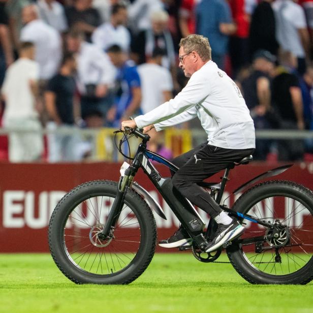 Ralf Rangnick fährt mit einem E-Bike über einen Fußballplatz