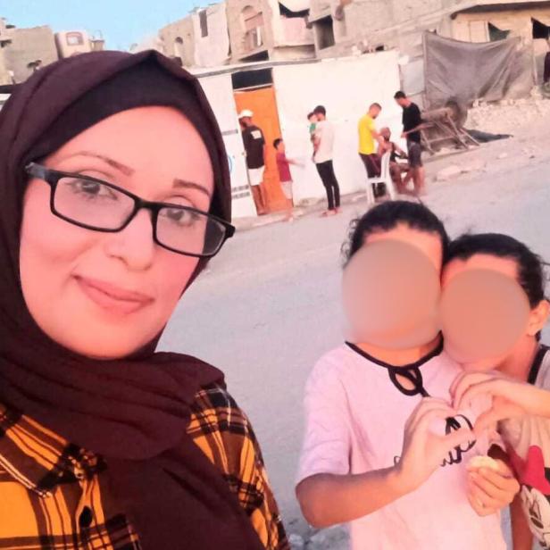 Eine Frau mit Kopftuch auf der Straße vor ihren zwei Kindern mit verpixeltem Gesicht