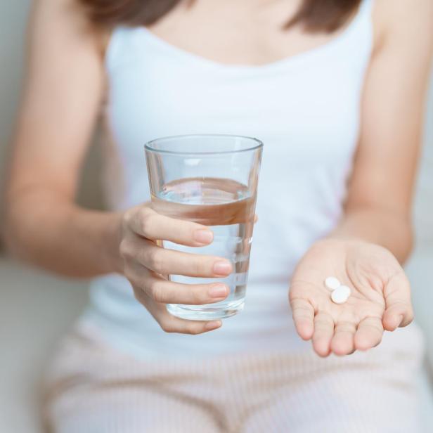 Eine junge Frau nimmt Medikamente zusammen mit einem Glas Wasser ein.